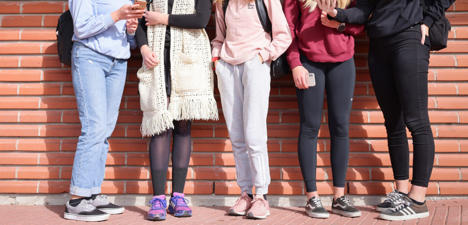 Nuoret seisovat seinää vasten ja katsovat puhelimiaan.