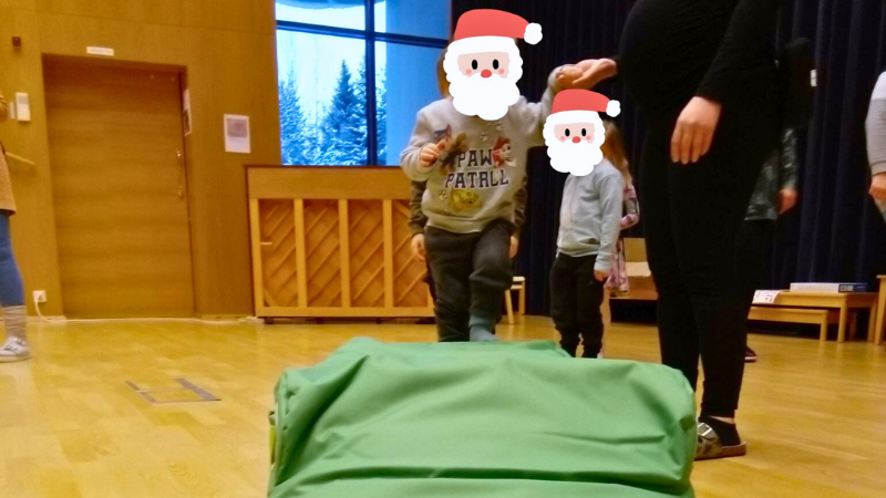 Päiväkodin hoitaja auttamassa lasta nousemaan säkkituolin päälle.