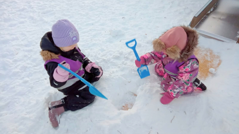 Kaksi lasta lumihangessa kaivamassa kuoppaa lelulapioilla.