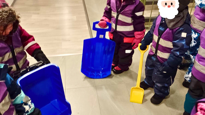 Päiväkotilapsia ulkovaatteissa porraskäytävässä, mukanaan liukureita ja lelulapioita.