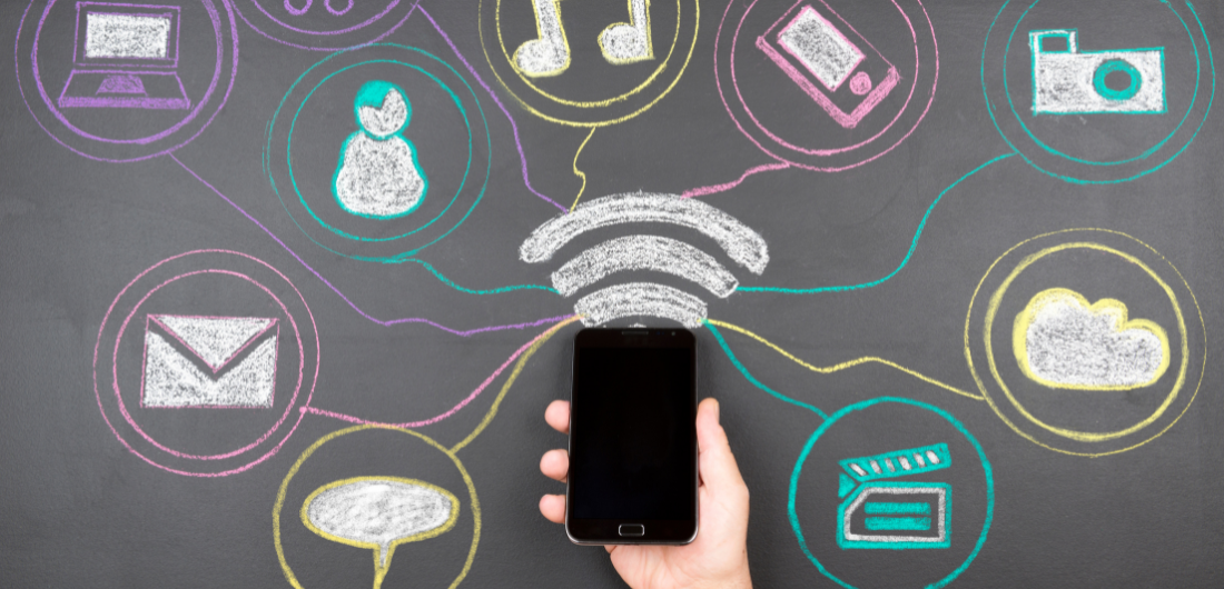 Kädessä oleva älypuhelin liitutaulutaustan edessä.