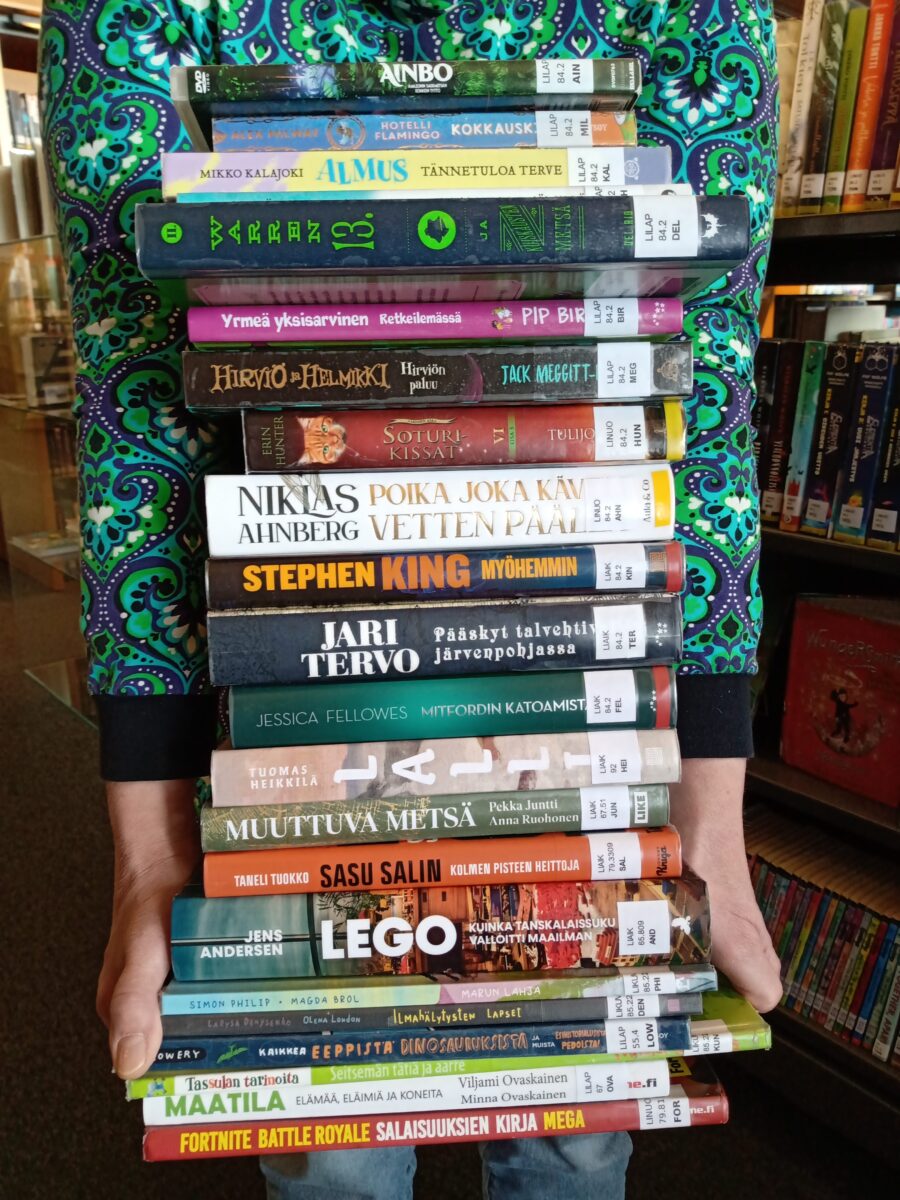 Kahdenkymmenenkahden kirjan pino sylissä