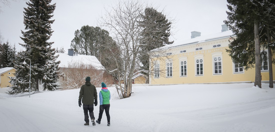 Mies ja nainen kävelevät lumisella Rantatiellä, Vilho Lampi-museon edessä.