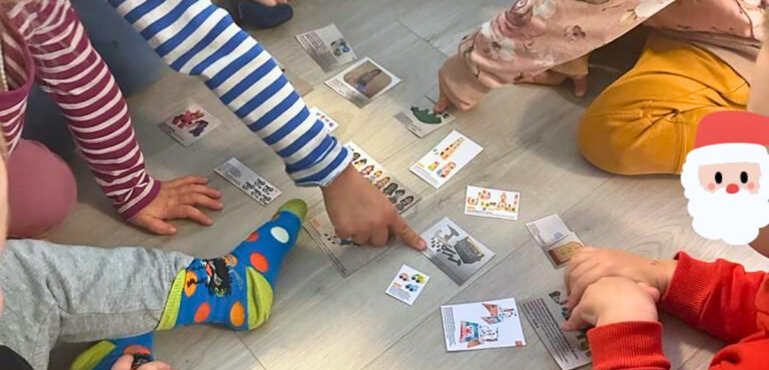 Lapsia kerääntynyt lattialle levitettyjen lelukuvien äärelle, kaksi lasta osoittaa eri kuvia.