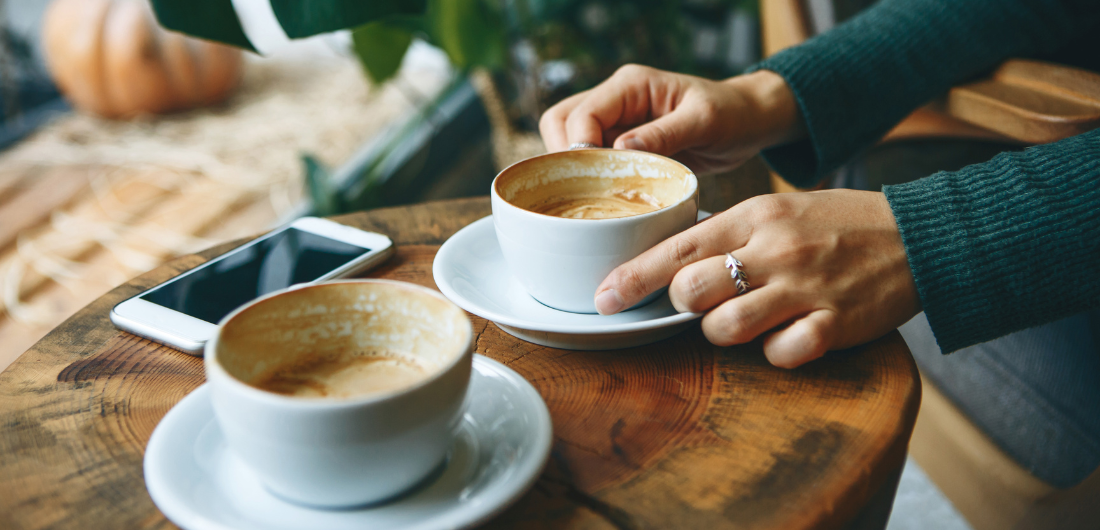 Kädet pitelevät kahvikuppia pöydän päällä.