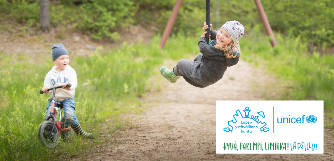 Kaksi lasta leikkii ulkona. Kuvan päällä Lapsiystävällinen kunta -logo