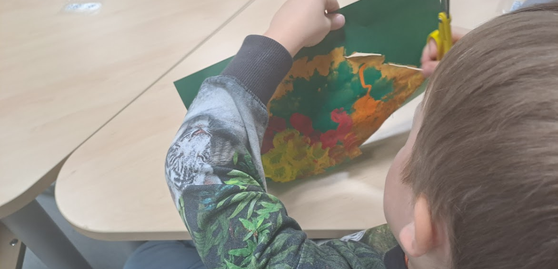 Lapsi leikkaa saksilla puun lehteä paperista.