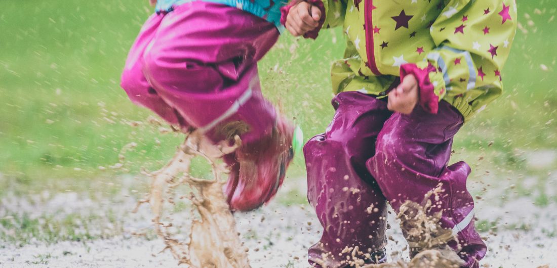 Kura-asuiset lapset hyppivät lätäkössä.