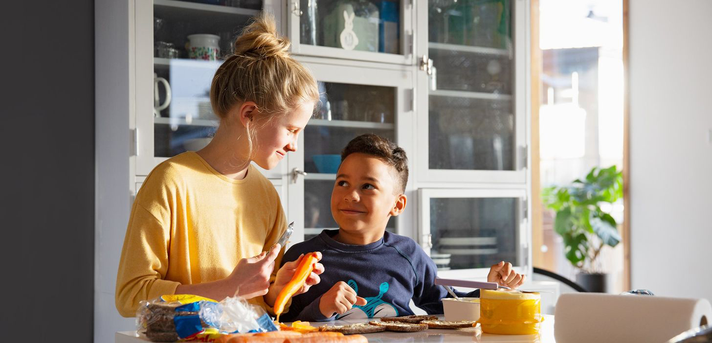 Kaksi lasta laittaa välipalaa keittiössä.