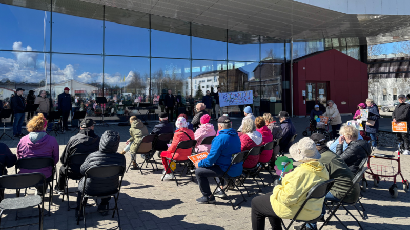 Valokuvassa rollaattorimarssin osallistujat kuuntelevat puheita Limingan kirjaston pihalla.