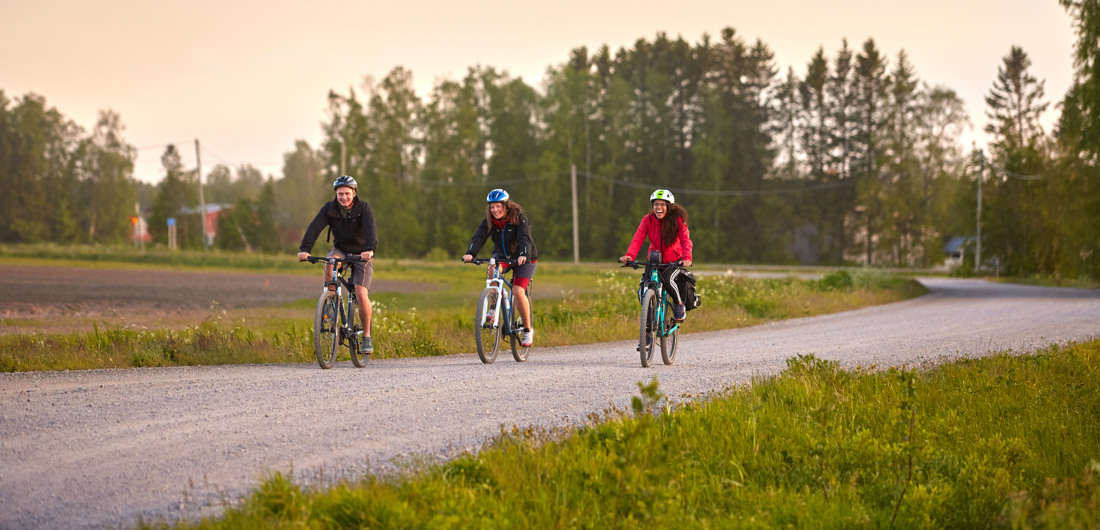 Kolme pyöräilijää pyöräilemässä soratietä pitkin kesällä.