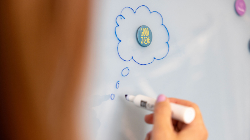Käsi piirtää valkotaululle ajatuskuplaa. Kuplan keskellä magneettinappi, jossa teksti "Good job".
