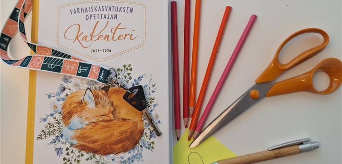 Varhaiskasvatuksen opettajan kalenteri, sakset ja kyniä pöydällä.