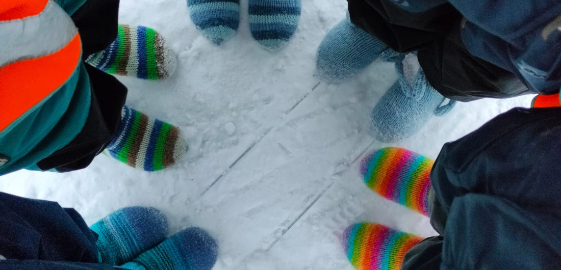 Ylhäältä päin kuvatussa kuvassa lasten villasukkien peittämiä jalkoja ringisssä lumihangella.