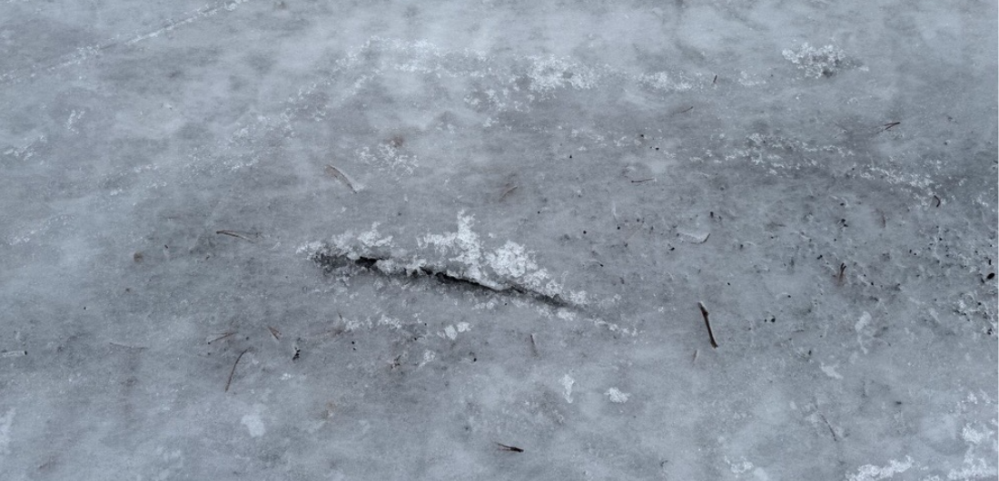 Jääpinnan lähikuva, jossa näkyy syvä halkeama ja epätasaisuutta sulamisen jäljiltä.