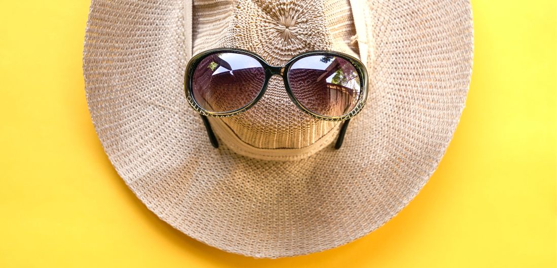 Aurinkohattu ja aurinkolasit keltaisella pohjalla.