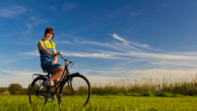 Tyttö pyöräilee peltomaisemassa.