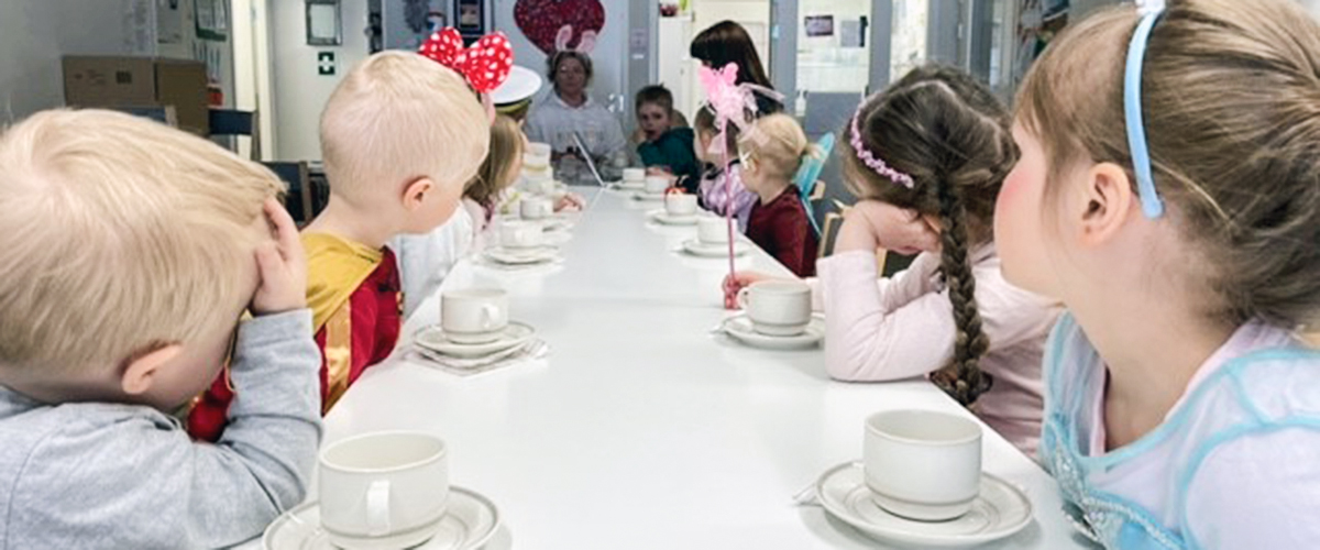 Lapset istuvat kokouspöydässä kahvikuppien kanssa.