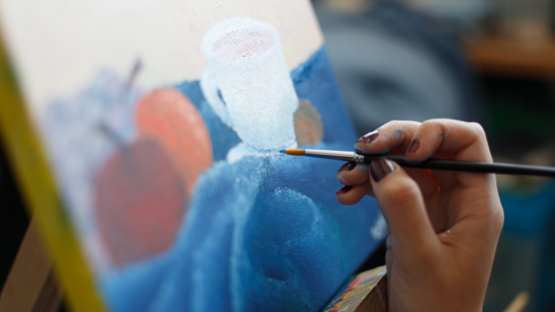 Käsi maalaa taulua pensselillä.