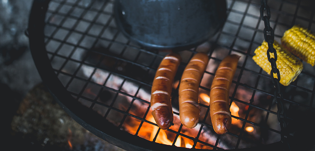 Nokikpannu, makkarat ja maissit nuotioritilän päällä.