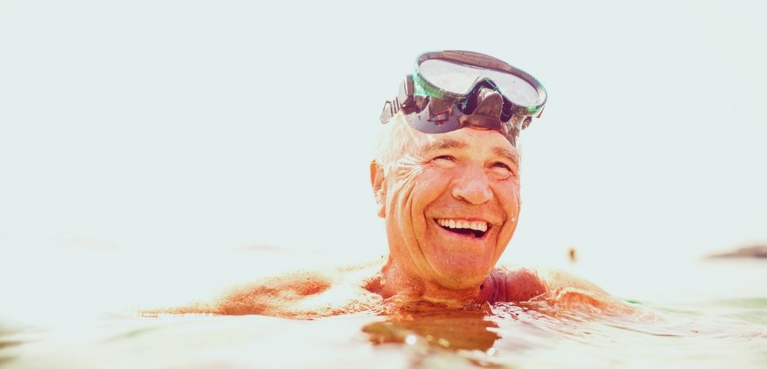 Mies on uimassa ja hymyilee uimalasit otsallaan.
