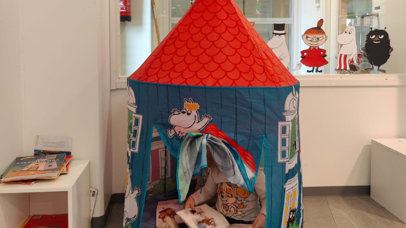 Lapsi lukee kirjaa muumitalon muotoisessa teltassa.