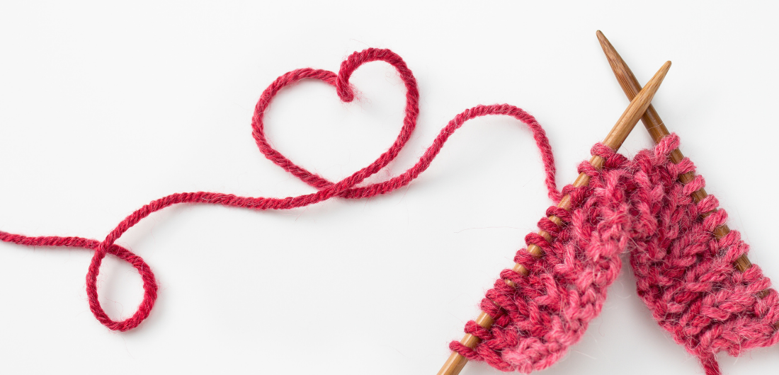 Neulomistyö pöydällä, punainen lanka muodostaa sydämen.