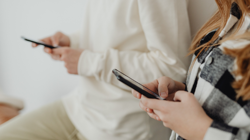 Kaksi nuorta selaa puhelimia ja nojaa seinään.