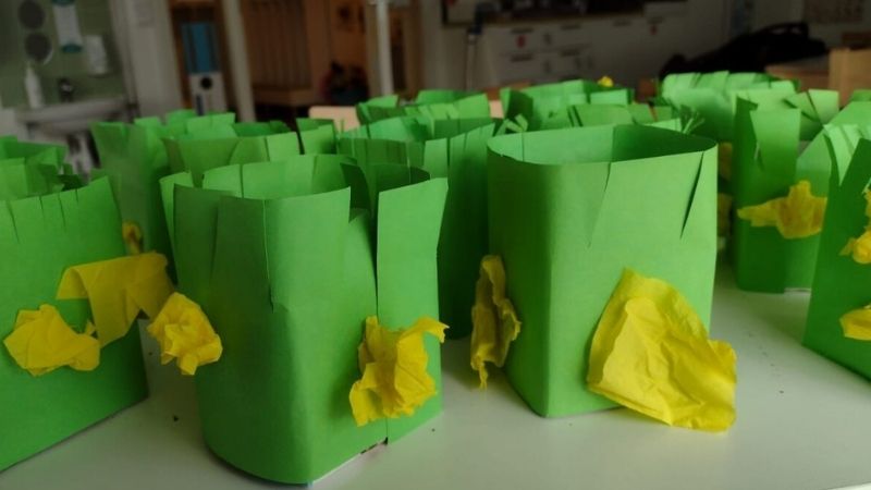 Maitopurkista askarreltuja, vihreällä paperilla päällystettyjä rairuohopurkkeja, joissa keltaista silkkipaperia koristeena.