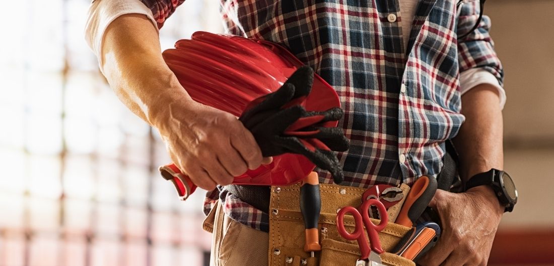 Rakennusmies seisoo kypärä kainalossa.