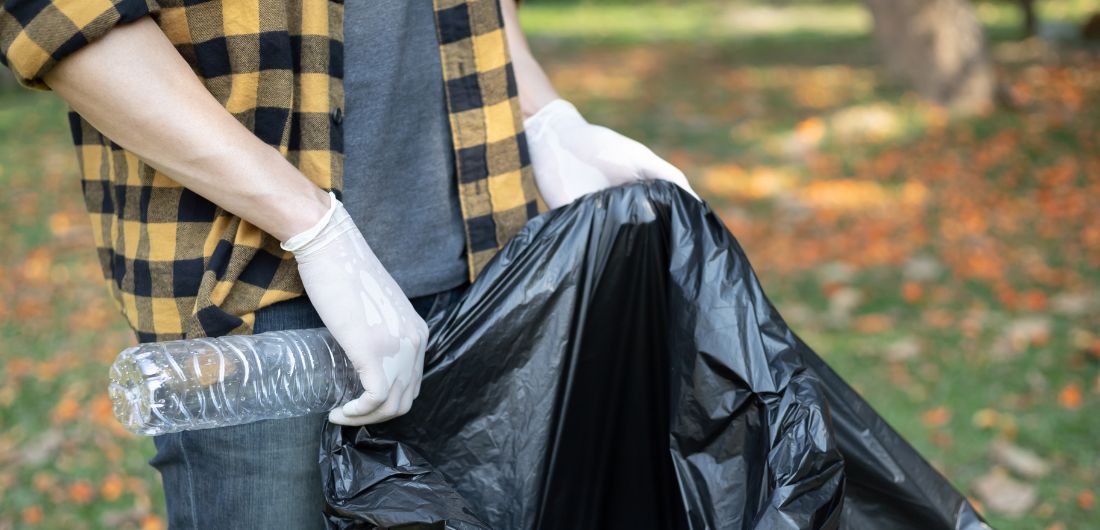 Ihmisen kädessä on jätesäkki, johon hän kerää roskia puistosta.