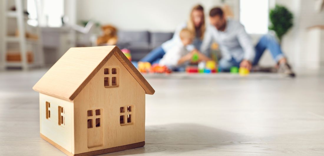 Pieni puinen mökki olohuoneen lattialla. Taustalla perhe.