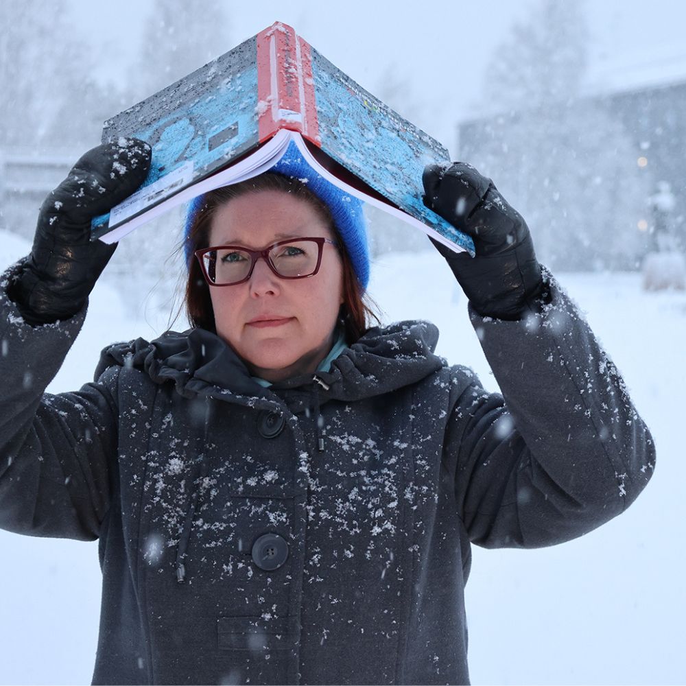 Nainen pitelee kirjaa päänsä päällä lumisateessa.