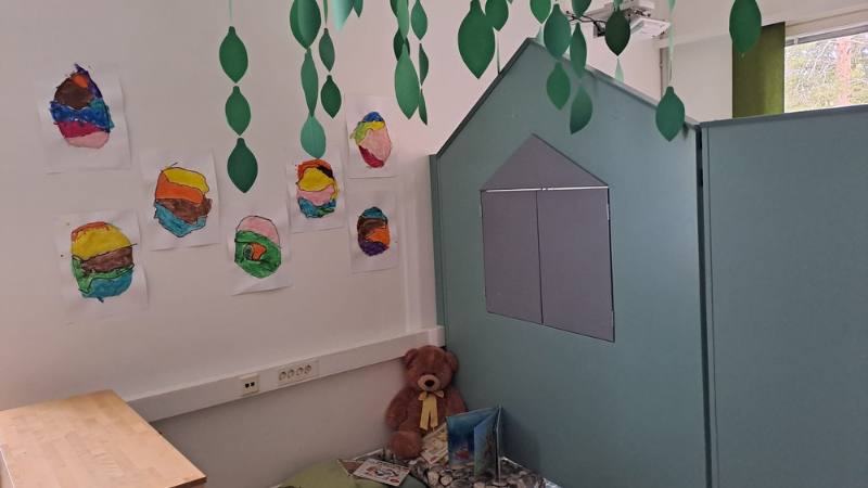 Katosta roikkuvia puunlehtiä ja lattialla nalle kirjojen kanssa.