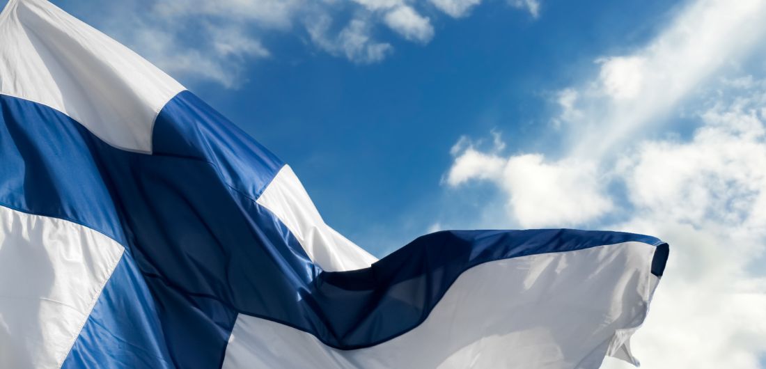 Suomen lippu liehuu sinitaivasta vasten.