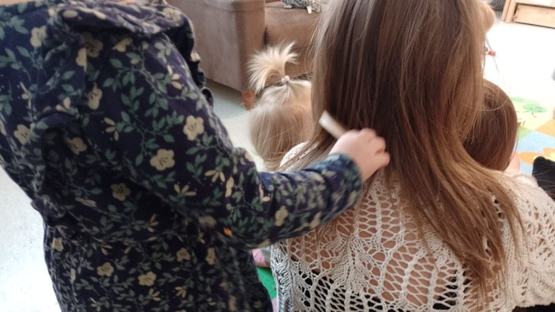 Kuvassa lapsi kampaa aikuisen hiuksia kampaamoleikissä.