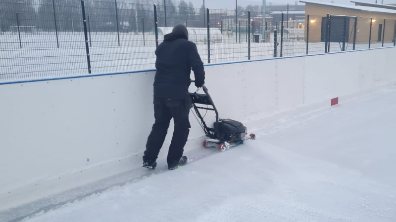 Henkilö hoitaa jääkiekkokaukalon reunoja reunajyrsimellä.