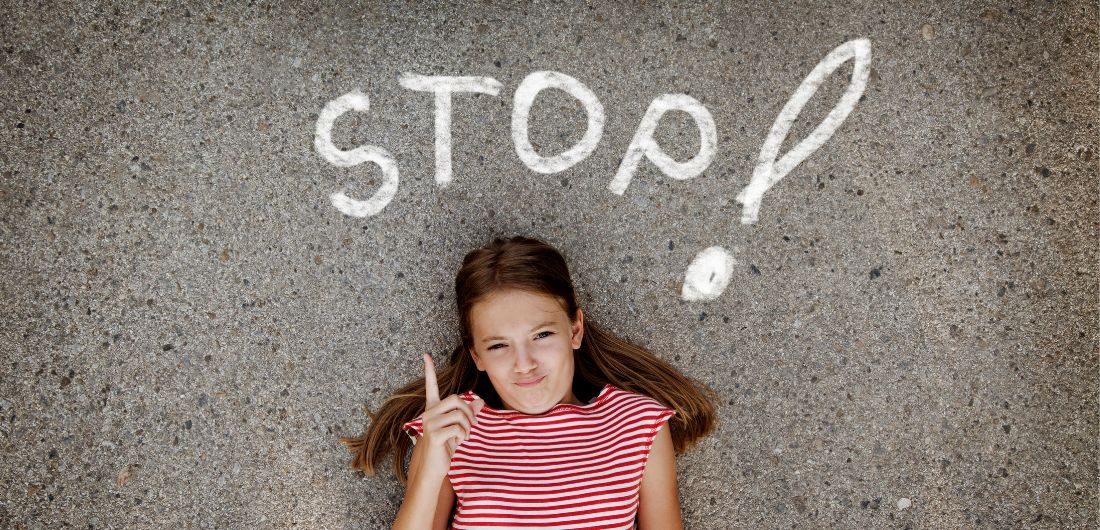 Tyttö heristää sormea ja asfaltissa lukee "Stop".